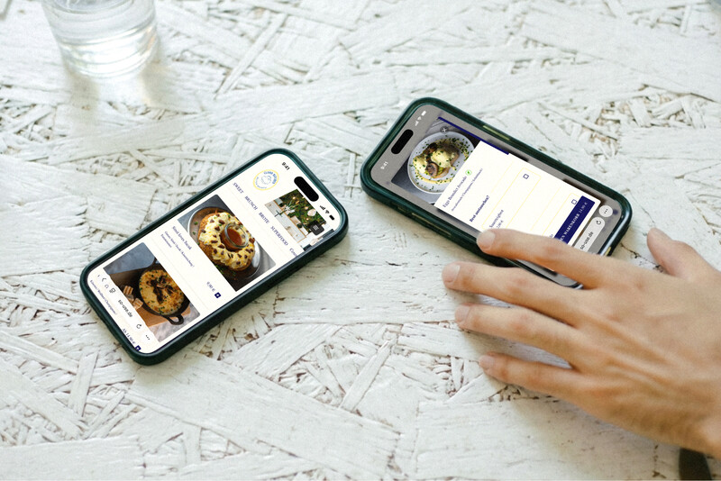 Zwei Smartphones, die eine digitale Speisekarte zur Essensbestellung anzeigen, liegen auf einem hellen Holztisch